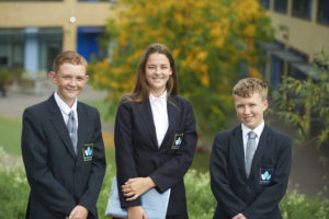 Three Longfield Academy students in uniform pose for the camera outside of the building.