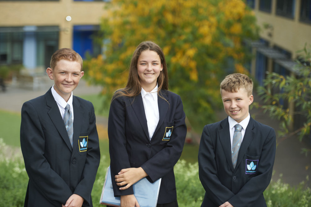 Three Longfield Academy students in uniform pose for the camera outside of the building.