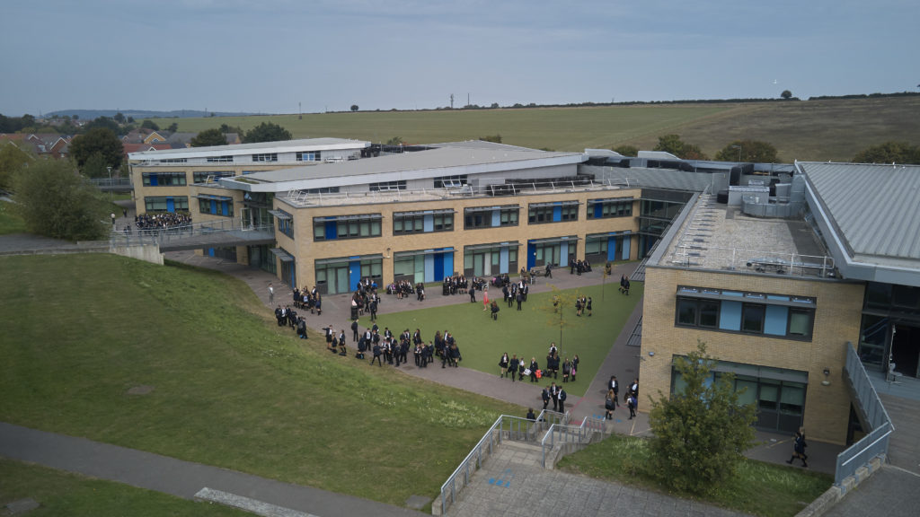 Photo of the outside of the Longfield Academy building, showing students walking around it.