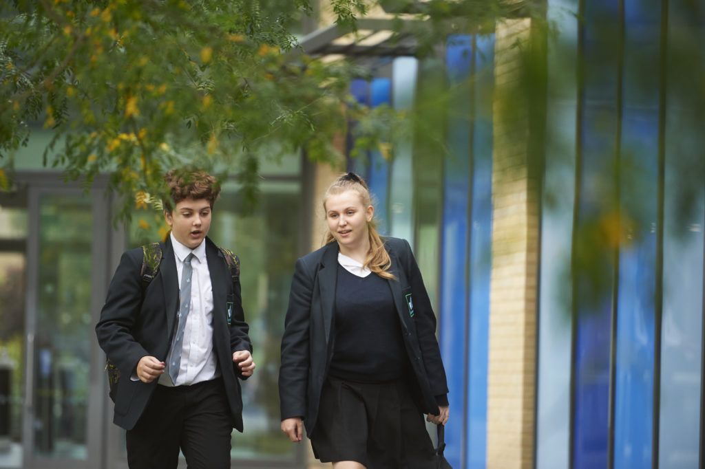Two Longfield Academy students, a boy and a girl, are seen walking alongside one another, outdoors on the academy grounds.