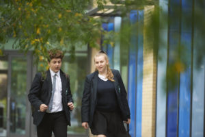 Two Longfield Academy students, a boy and a girl, are seen walking alongside one another, outdoors on the academy grounds.