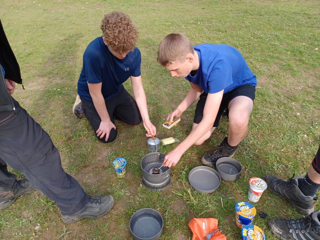 Two students are seen working together to light a portable stove and cook dinner for the group during a Duke of Edinburgh Practice Event.