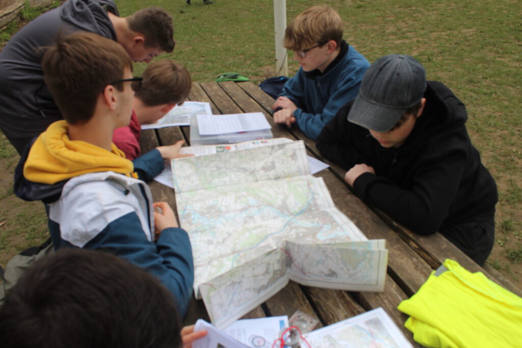 A group of students are seen looking at some maps together at a wooden table during a practice Duke of Edinburgh event.