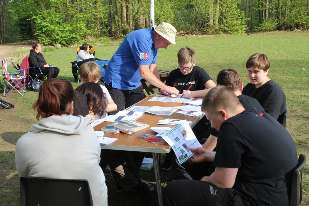 A staff member is seen assisting a group of students sat at a desk outdoors during a Duke of Edinburgh practice event.