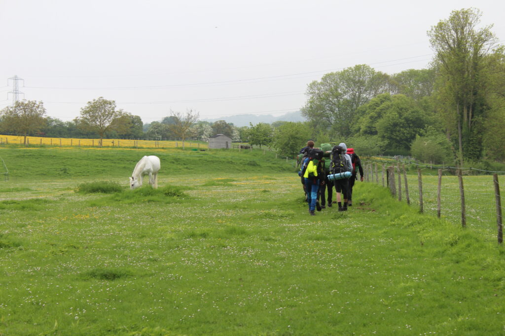 A group of students are pictured walking across a field with a horse to the left of them during a DofE practice event.