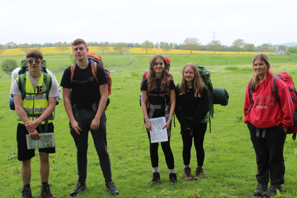 Five students are pictured smiling for the camera, wearing their backpacks during a DofE practice event in 2023.