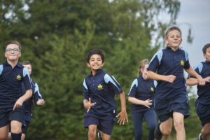 A group of six Longfield Academy students are seen running across a field together in their PE Kit, smiling for the camera as they go.
