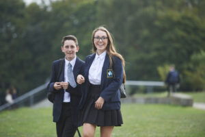 Two Longfield Academy students, a boy and a girl, are pictured walking together in their academy uniform and smiling for the camera.