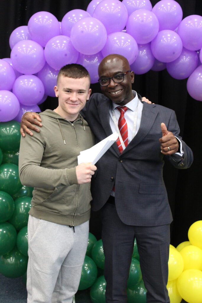 A male student is seen smiling for the camera, alongside the Principal on GCSE Results Day 2023.