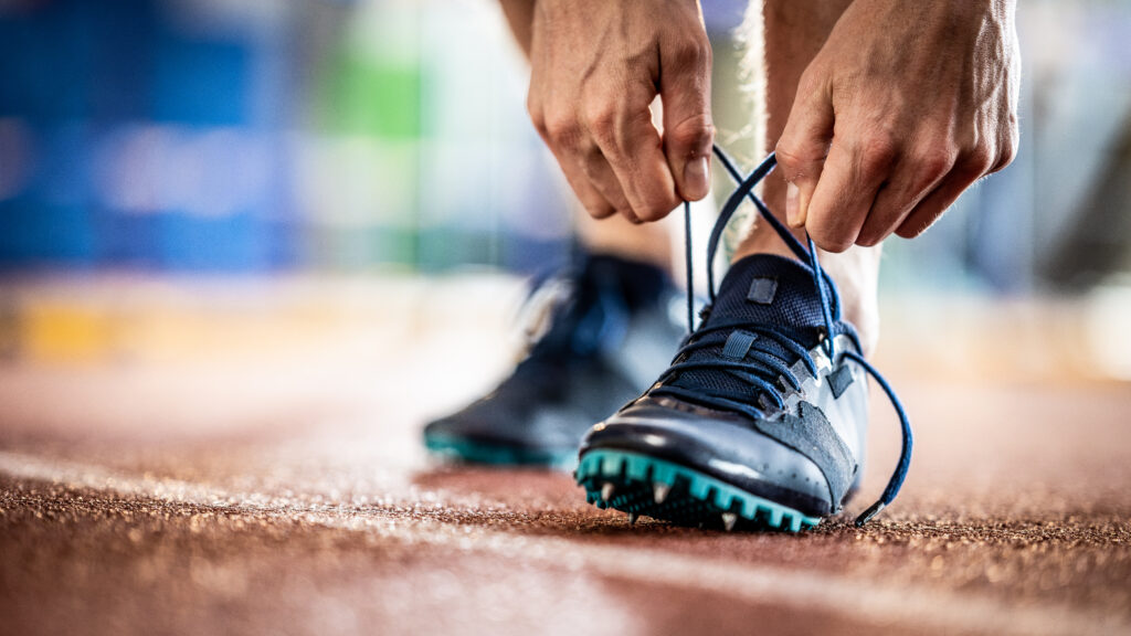 A pair of hands are pictured reaching down to tie the laces on an athlete's running trainers.