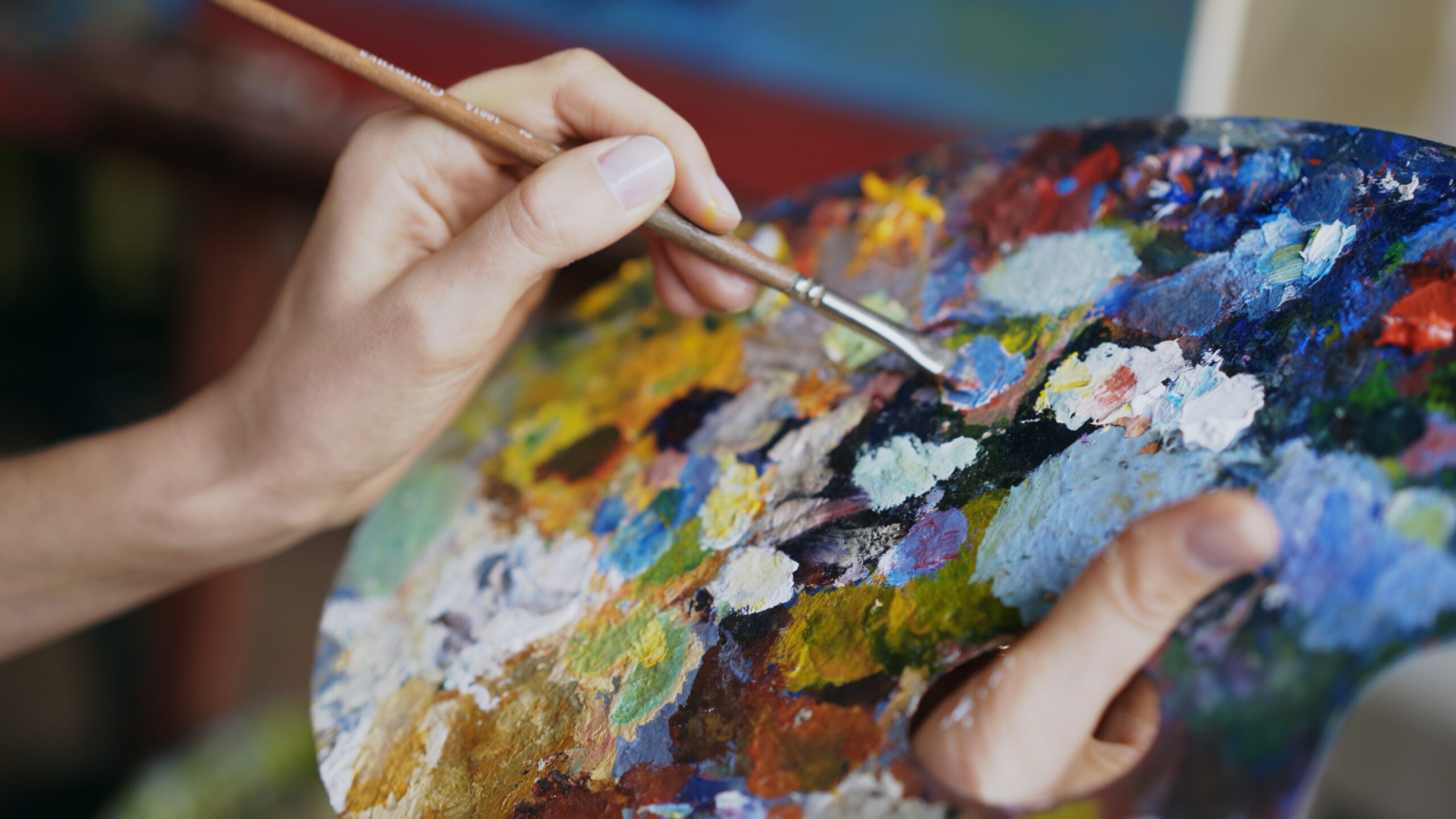 Close up of woman's hand mix paints with brush in palette in art-class indoors
