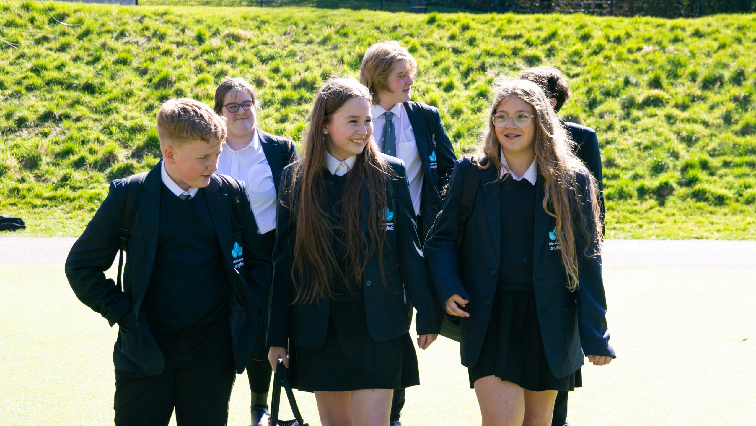 Students stood in 2 rows in front of a hedge smiling